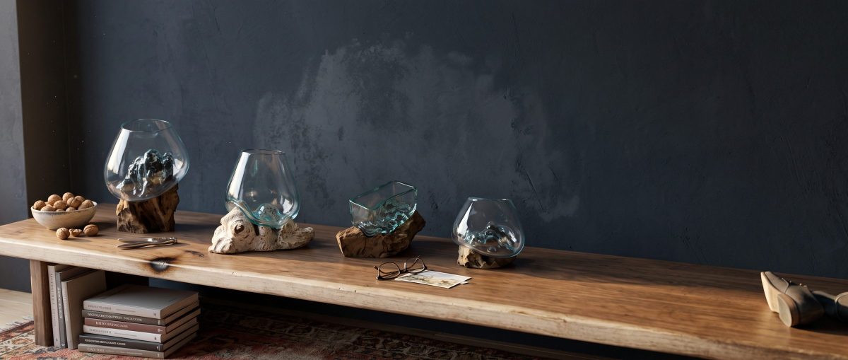 Quatre coupes en verre soufflé sur un banc de bois clair devant un mur ardoise, un bol de noix et des livres empilés