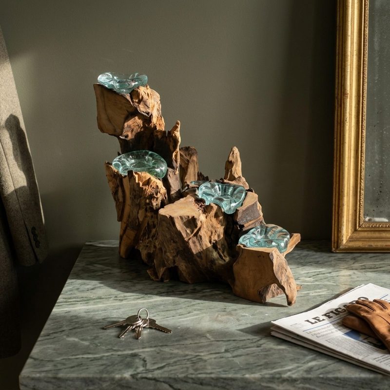 Chandelier cinq flammes en verre soufflé posé sur une console en marbre vert sous un miroir doré, trousseau de clés et journal plié à côté